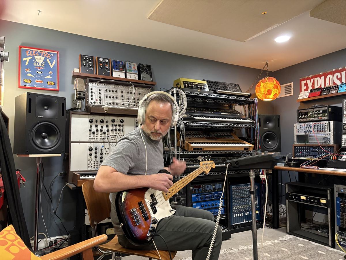 The bass player tracking in headphones in front of a wall of modular synths