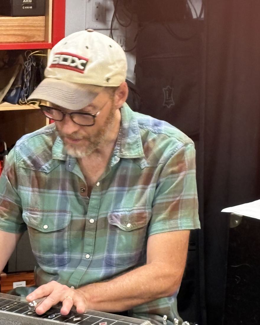 The band’s pedal steel player, in a ball cap and plaid shirt, playing in the studio