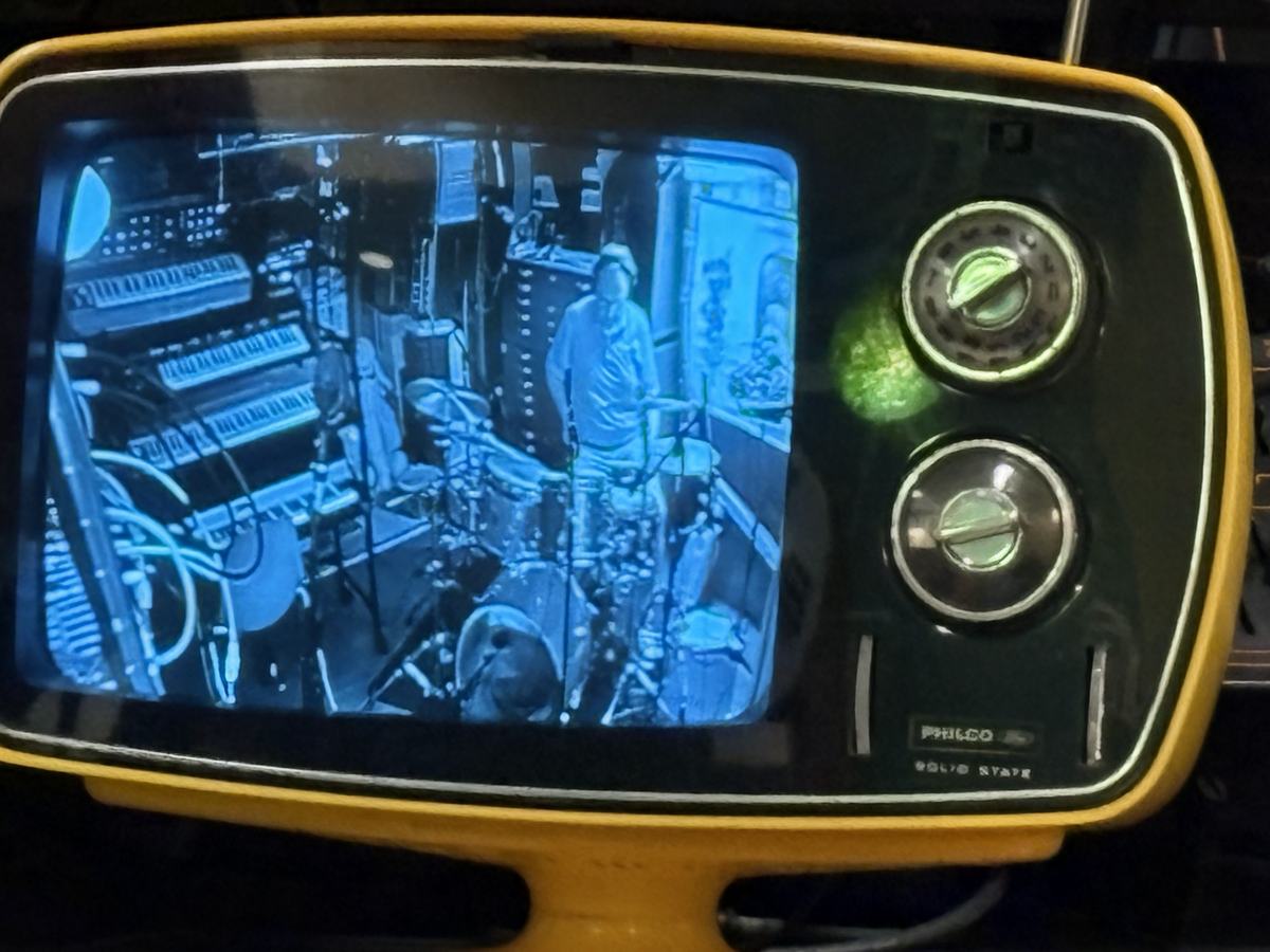 A vintage yellow Philco TV monitor showing a black and white view of the studio